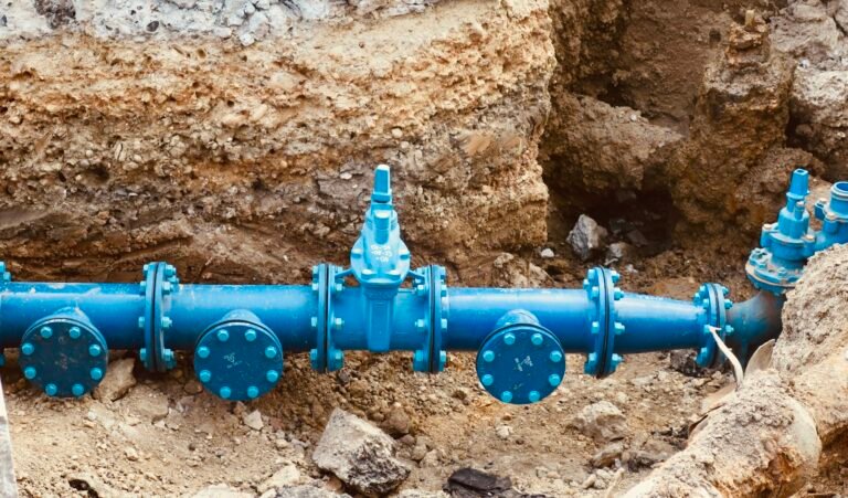 Exposed blue water main with valves running through an excavated trench
