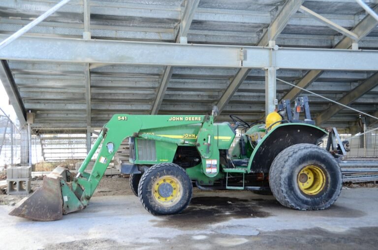 Compact utility tractor with a front loader parked under a steel shed