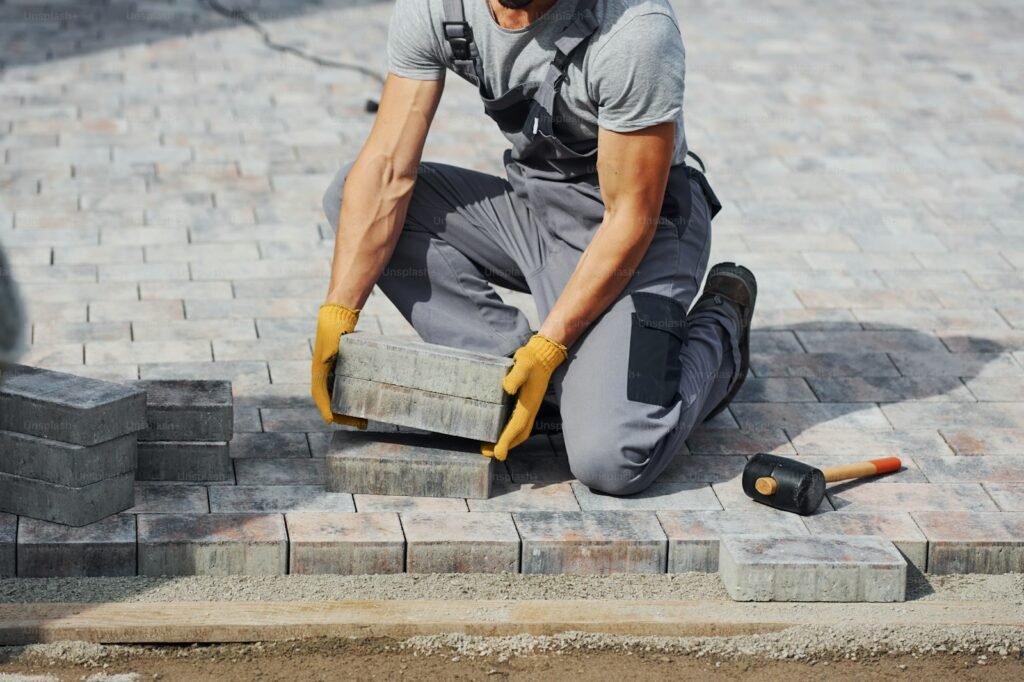 Worker in gloves laying grey block paving on a new driveway base