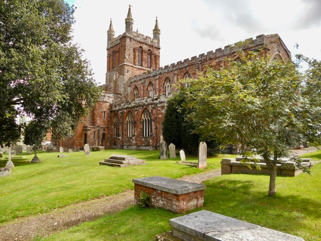 Red sandstone Holy Cross Church in Crediton with its churchyard and trees on a sunny day