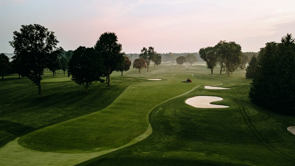 Early-morning golf course with bunkers and fairways as a maintenance vehicle works in the distance