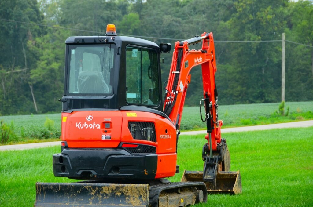 Orange rubber-tracked mini excavator parked on a grass verge, ready for hire