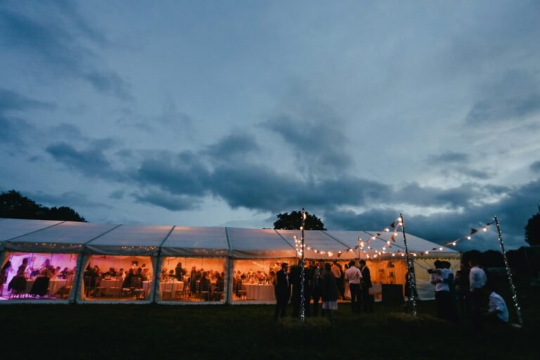 Lit white marquee with festoon lights in a field at dusk