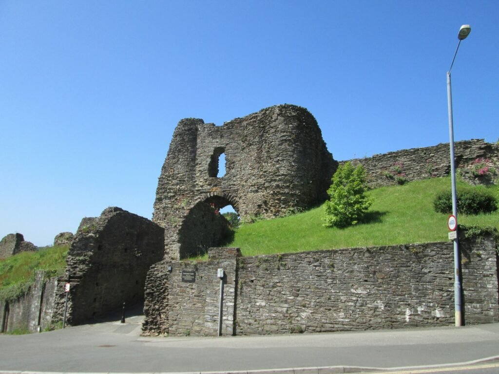 Ruined stone gatehouse of Launceston Castle above a roadside wall on a sunny day