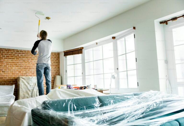 Sofa and furniture wrapped in plastic sheeting while a decorator paints the ceiling