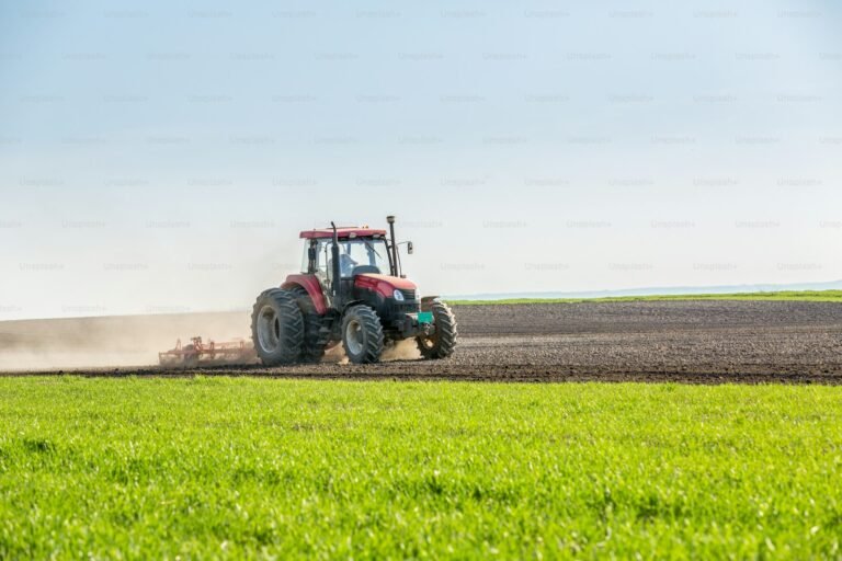 Red tractor pulling a cultivator across freshly worked arable land