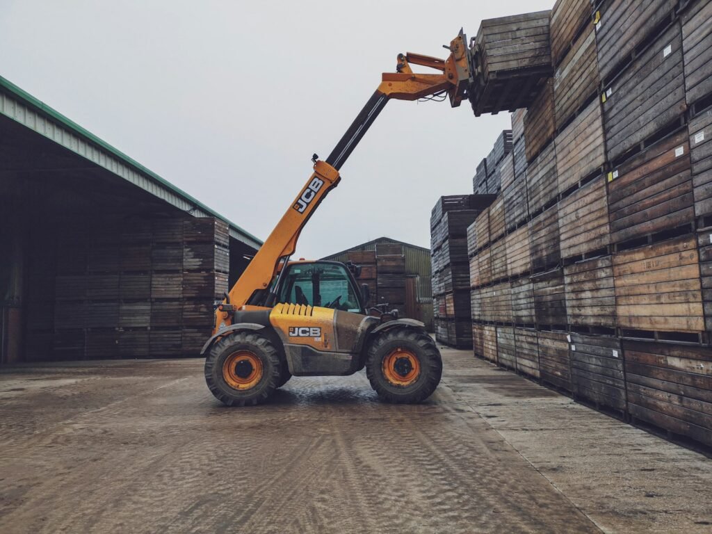 Telehandler with boom raised beside stacks of timber in a yard