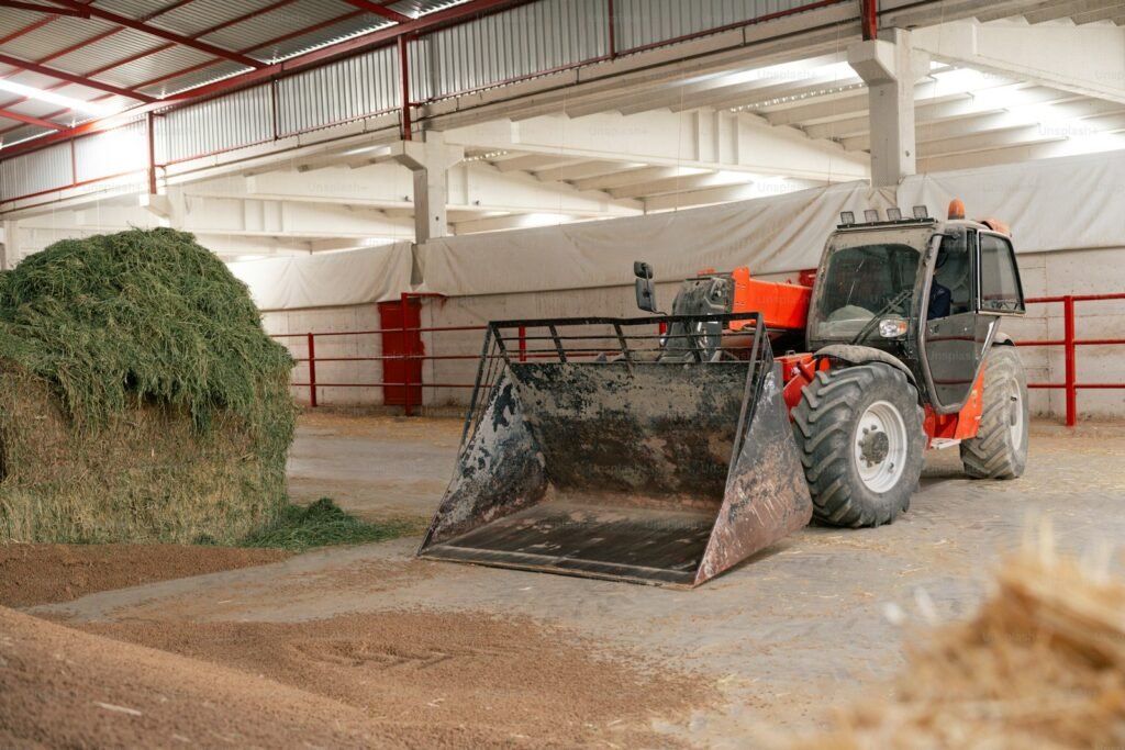 Compact telehandler with a bucket next to a pile of hay in a farm barn