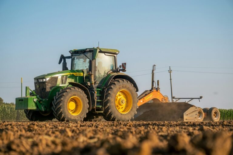 Green John Deere tractor working a ploughed field with an implement